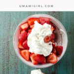 balsamic strawberries topped with whipped cream in a white bowl with a spoon on a blue background