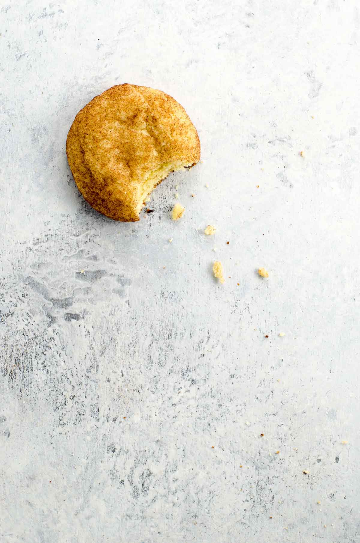 a chewy snickerdoodle on a light background with crumbs and a bite taken out of it