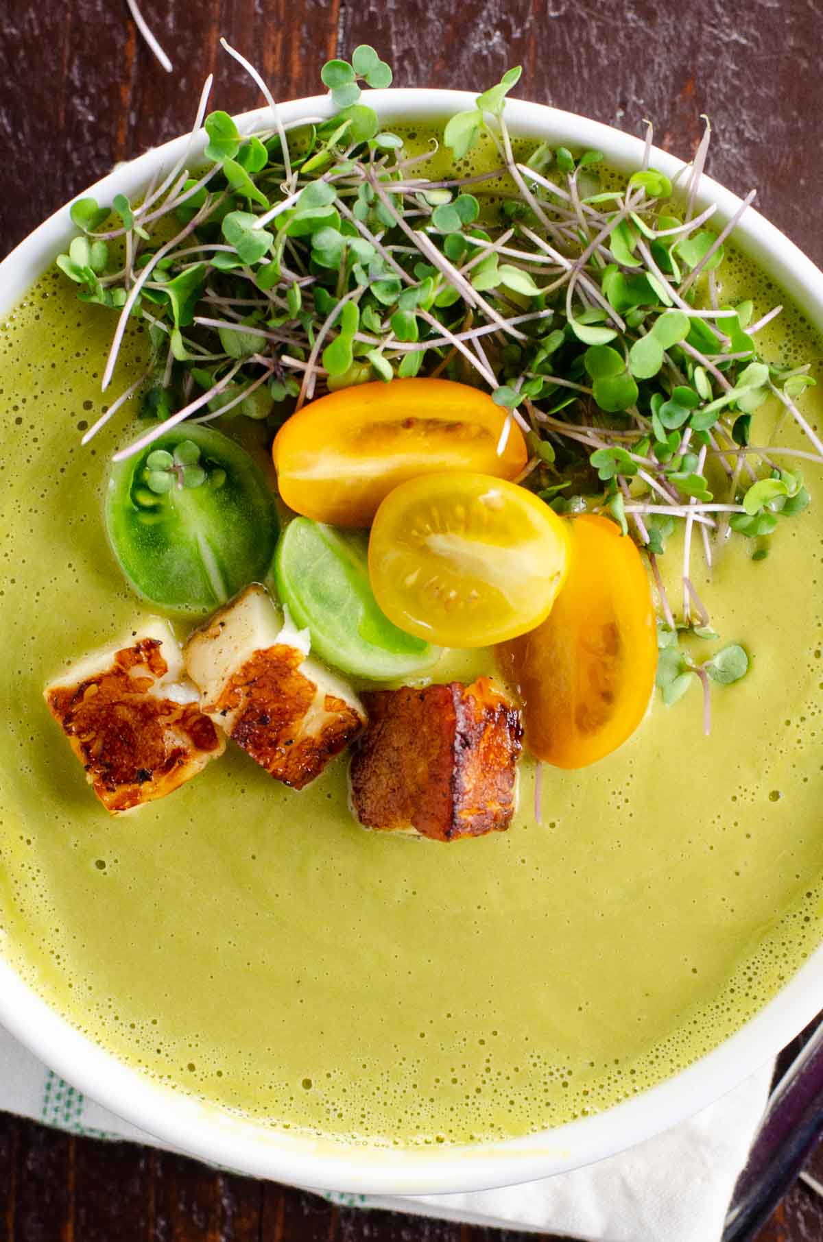 creamy asparagus ramp soup in a white bowl with halloumi, tomato, and microgreen garnish