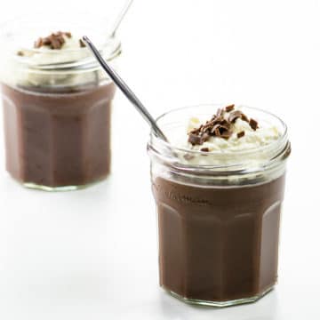chocolate pudding with whipped cream and chocolate shavings in two jam jars with spoons