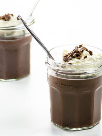 chocolate pudding with whipped cream and chocolate shavings in two jam jars with spoons