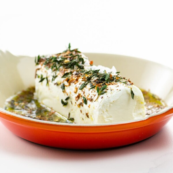 marinated goat cheese appetizer with olive oil and spices in an orange serving dish