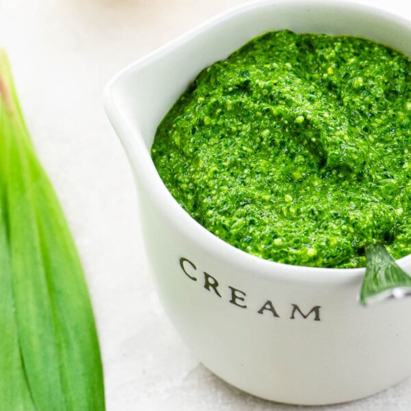 ramp pesto in a small pitcher with ramp leaves, a lemon, and pine nuts