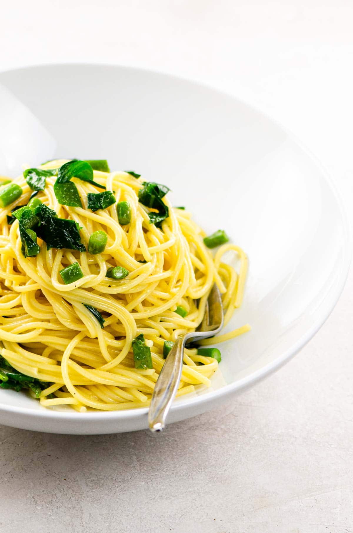 vegetarian spaghetti carbonara with asparagus and ramps in a white bowl