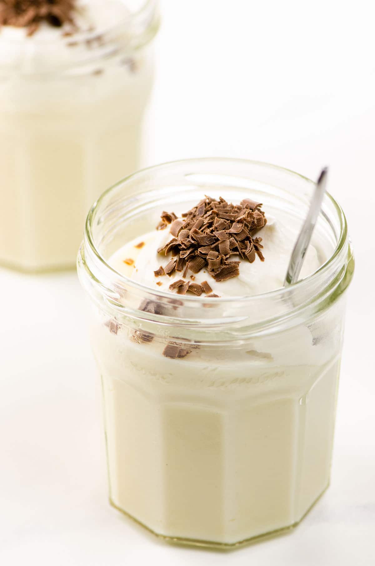 classic vanilla pudding with whipped cream and chocolate shavings in two jam jars with spoons