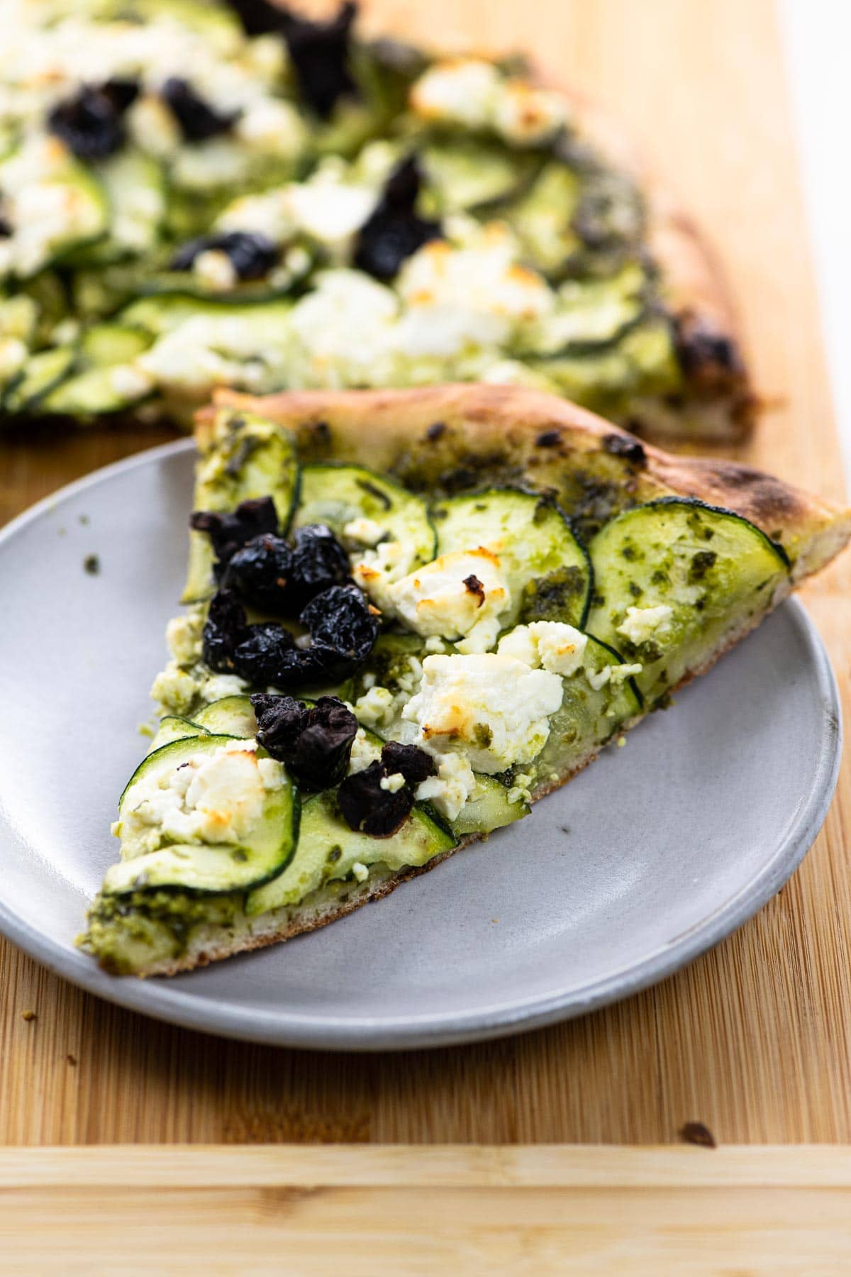 pesto and feta pizza with zucchini and black olives on a pizza peel and a plate