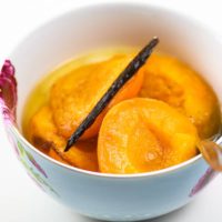 poached apricots with a vanilla bean in a blue bowl