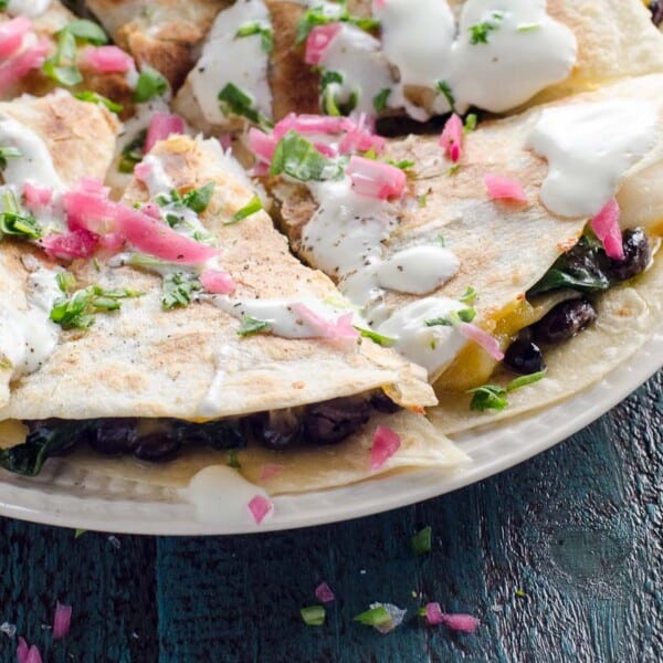 a shrimp quesadilla with spinach topped with sour cream, pickled onions, and scallions on a blue background