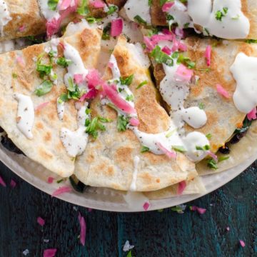 a shrimp quesadilla with spinach topped with sour cream, pickled onions, and scallions on a blue background