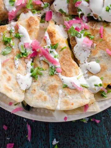 a shrimp quesadilla with spinach topped with sour cream, pickled onions, and scallions on a blue background