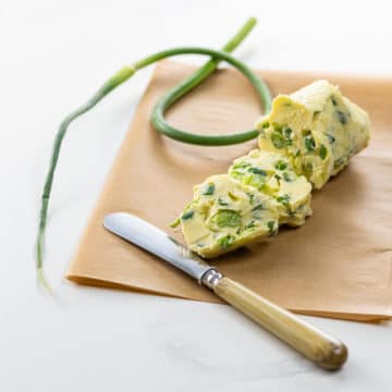 garlic scape butter on parchment with a small knife and a garlic scape