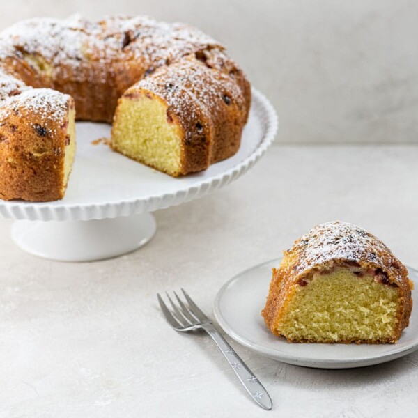 a slice of sour cherry cake on a plate with the rest of the cake on a stand behind it