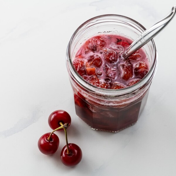 sour cherry syrup in a small jar with a spoon and three cherries