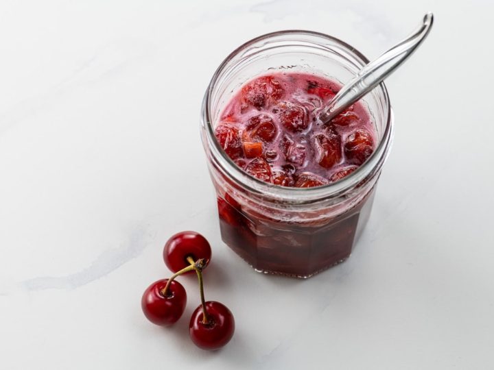 sour cherry syrup in a small jar with a spoon and three cherries