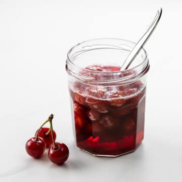 sour cherry syrup in a small jar with a spoon and three cherries
