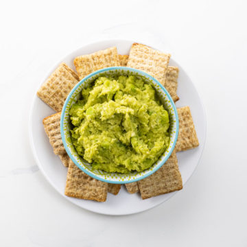 a bowl of fava bean puree with crackers on a plate