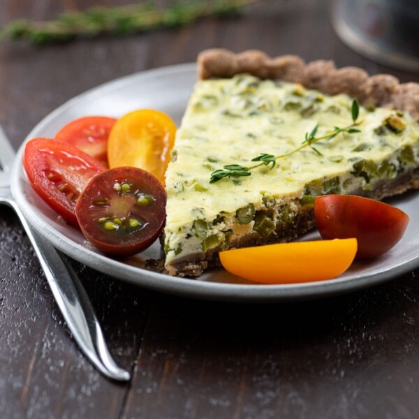 garlic scape tart with teff crust on a plate with tomatoes and a coffee cup