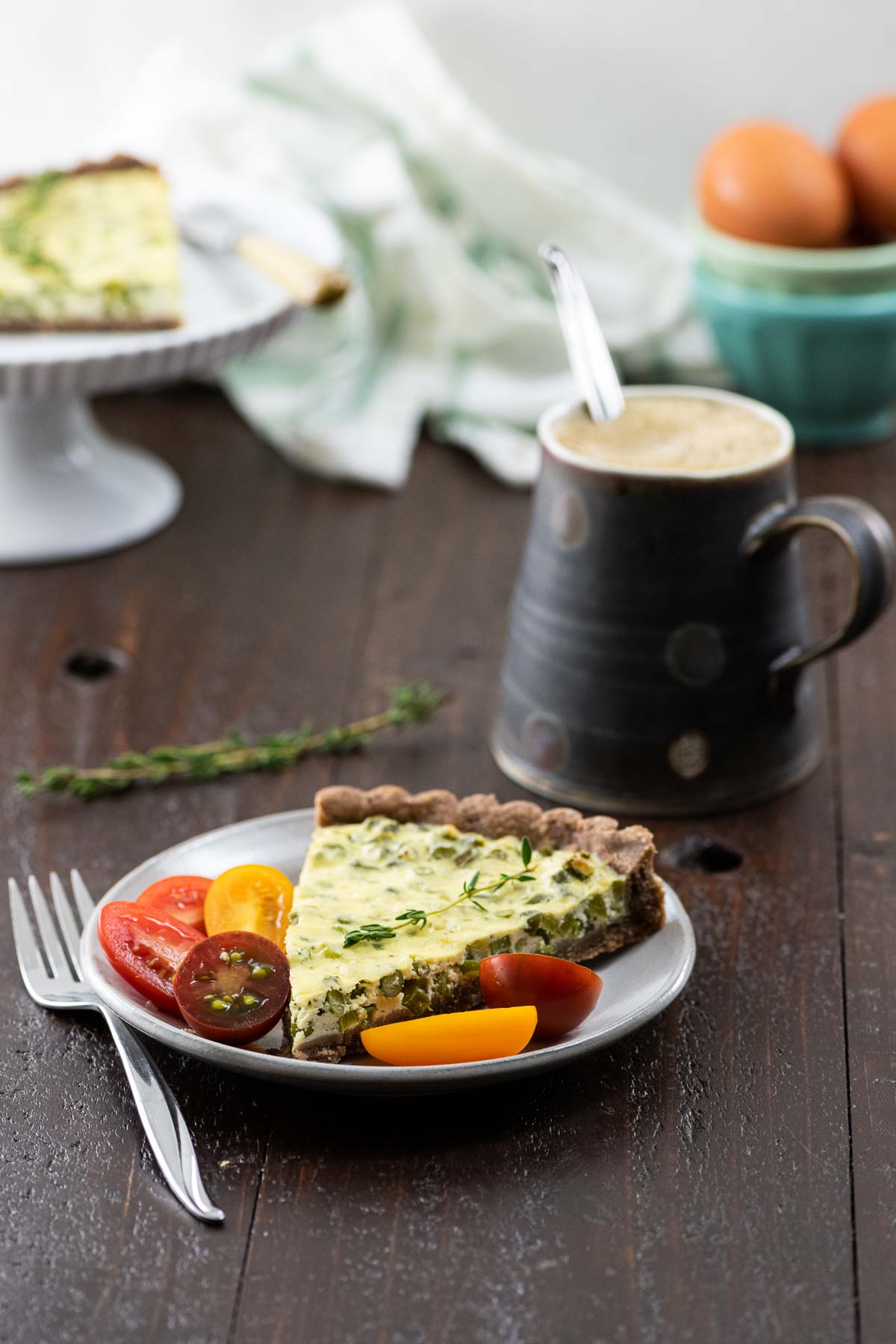 garlic scape tart with teff crust on a plate with tomatoes and a coffee cup