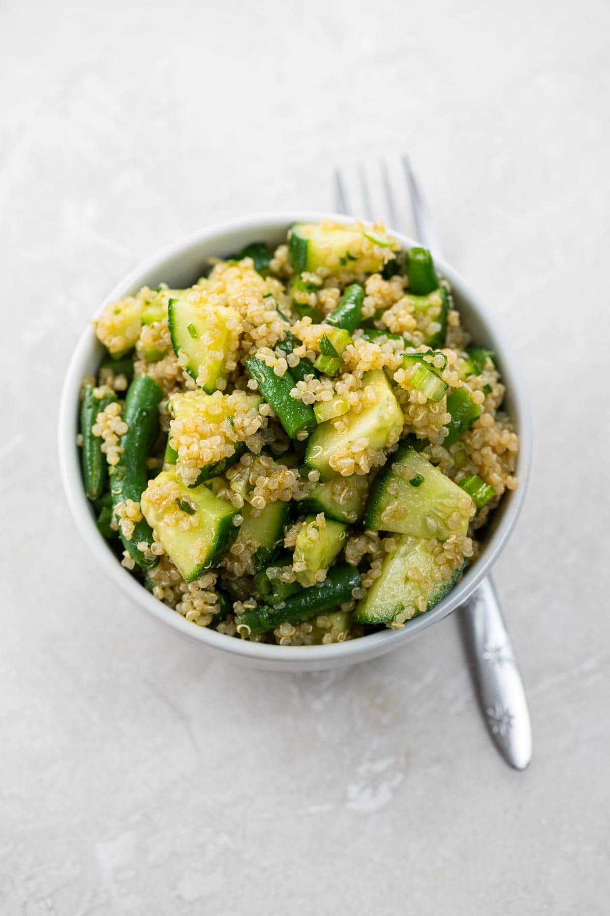 a bowl of quinoa salad with green vegetables and a fork
