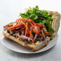 pork banh mi sandwich with pickled vegetables and cilantro on a white plate