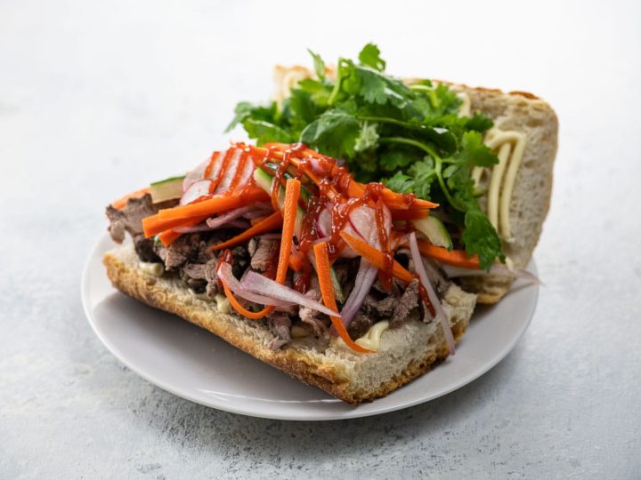 pork banh mi sandwich with pickled vegetables and cilantro on a white plate