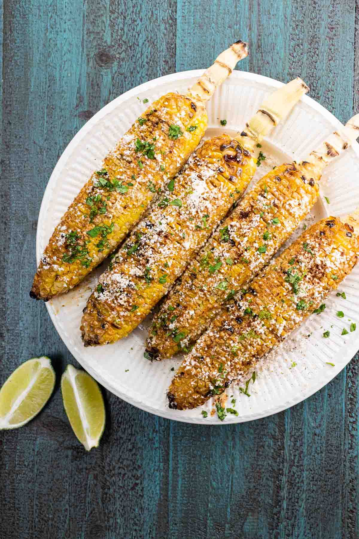 four ears of mexican street corn on a plate with lime wedges