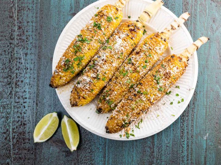 four elotes on a plate with lime wedges