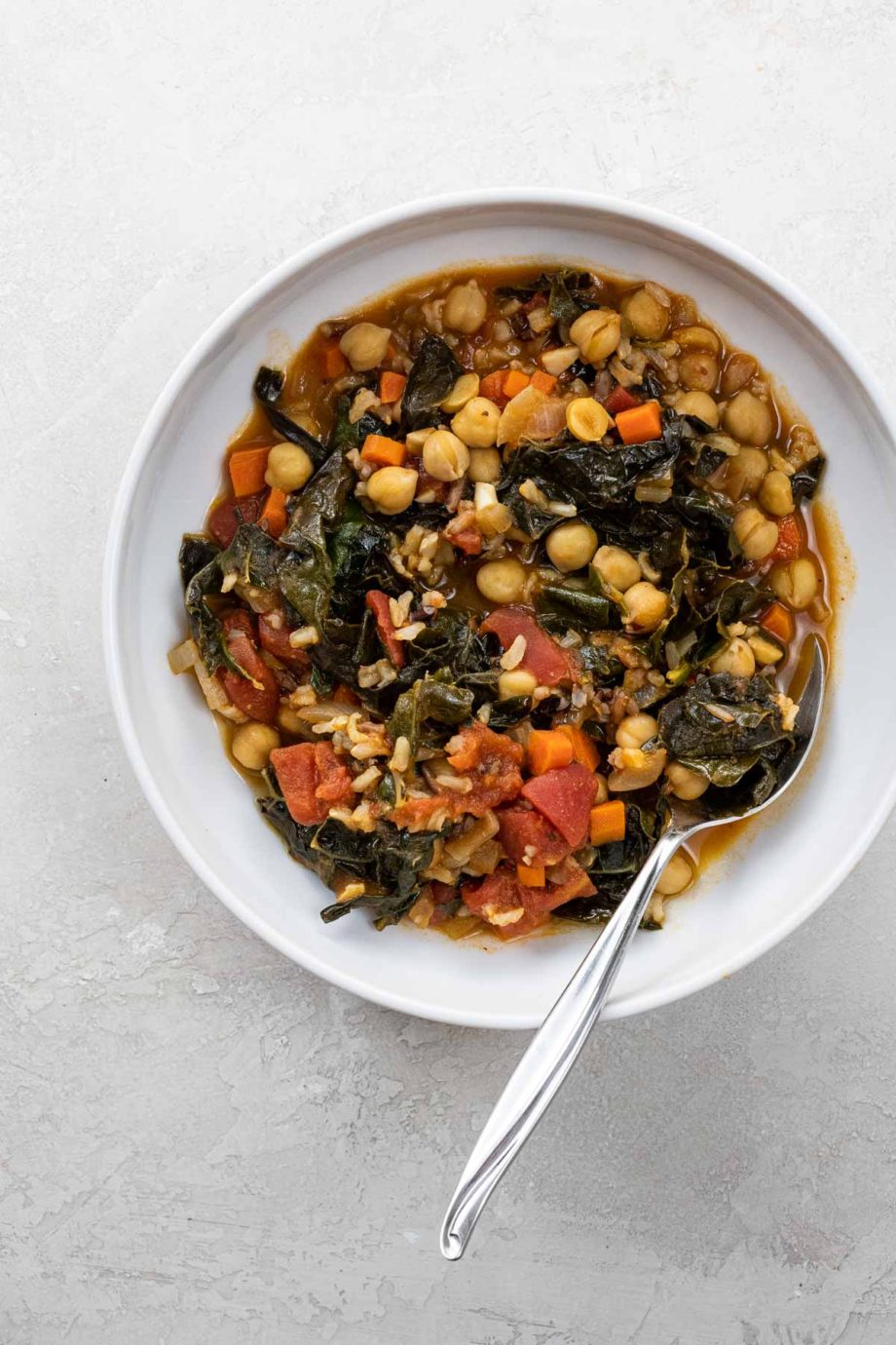 kale and chickpea stew in a white bowl with a spoon