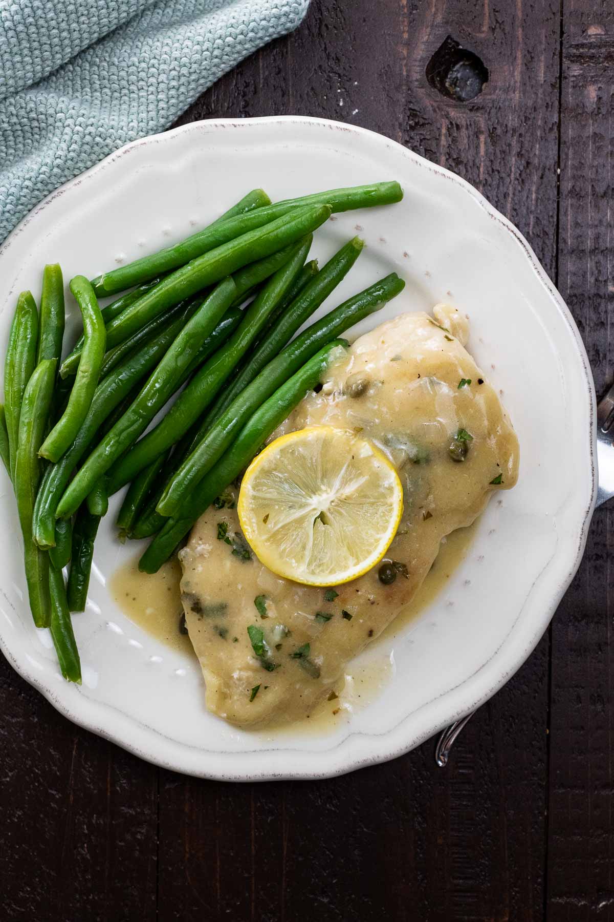 extra saucy chicken piccata on a plate with green beans and a lemon slice