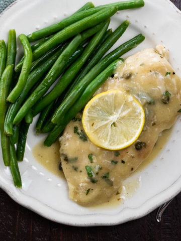 extra saucy chicken piccata on a plate with green beans and a lemon slice