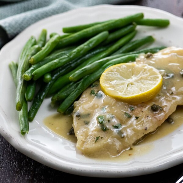 extra saucy chicken piccata on a plate with green beans and a lemon slice