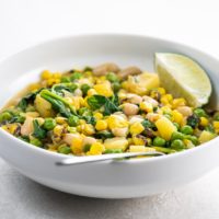 white bean stew with potatoes and corn in a white bowl with a spoon