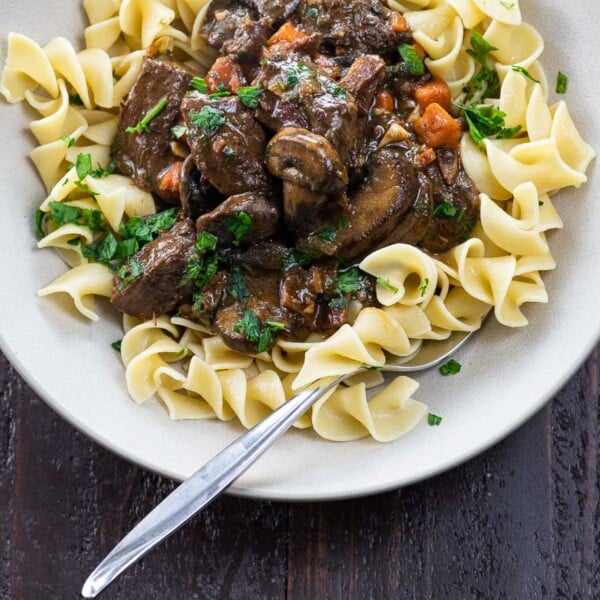 bouef bourguignon over egg noodles in a bowl with a fork