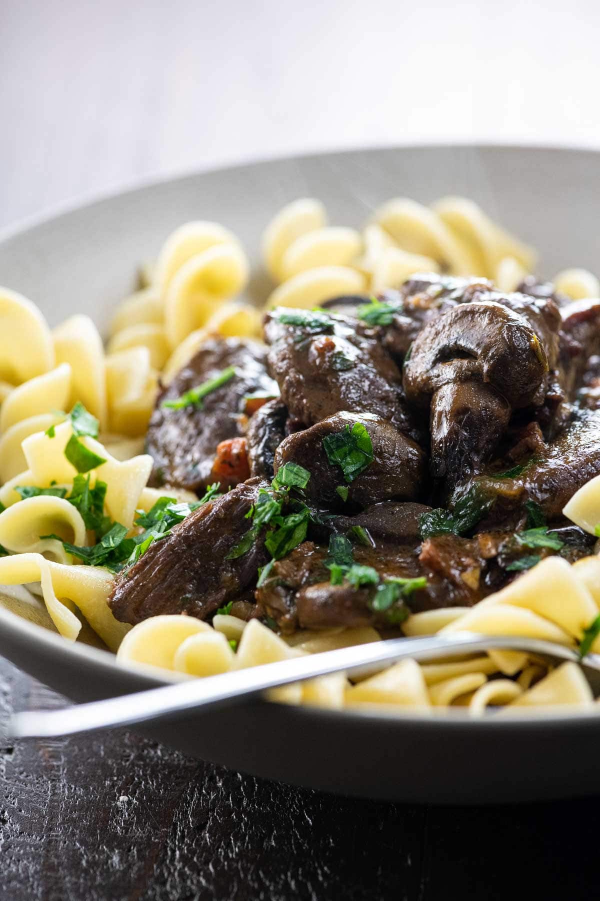 bouef bourguignon over egg noodles in a bowl with a fork