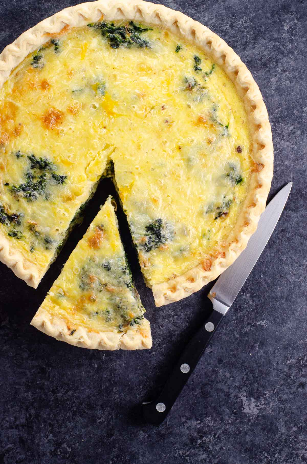 quiche florentine (spinach quiche) with a  slice cut out and a small knife