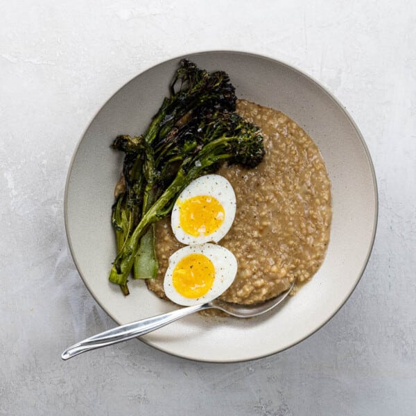 savory steel cut oats with a seven minute egg and crispy broccolini in a bowl with a spoon