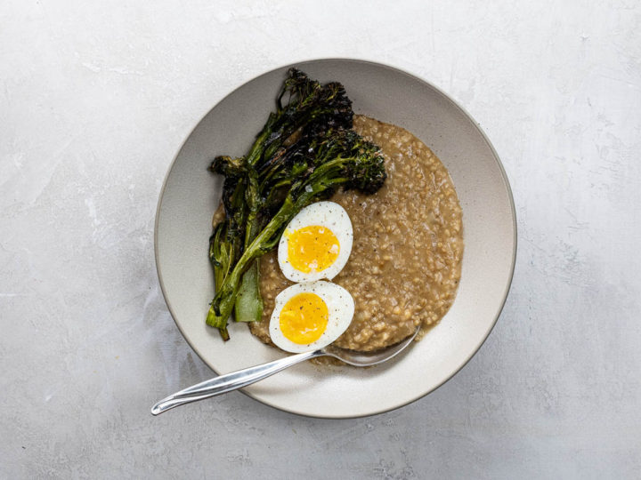 savory steel cut oats with a seven minute egg and crispy broccolini in a bowl with a spoon