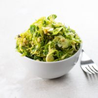 shredded brussels sprouts salad with pine nuts and pecorino in a white bowl with a fork