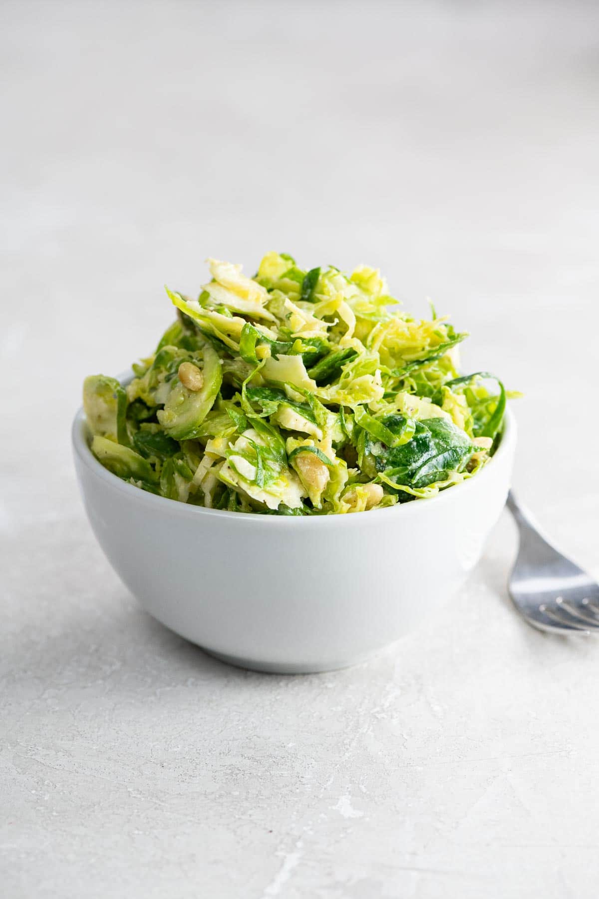 shredded brussels sprouts salad with pine nuts and pecorino in a white bowl with a fork