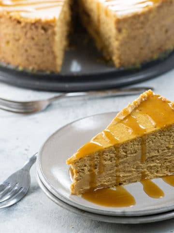 a slice of spiced pumpkin cheesecake on a plate with the rest of the cake in the background