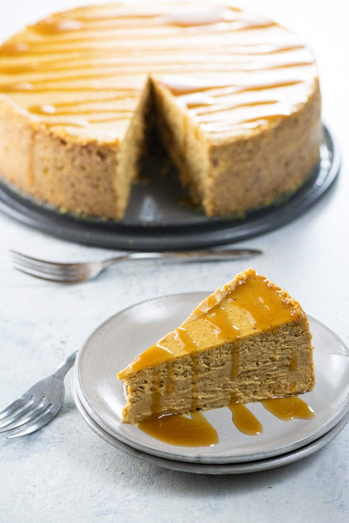 a slice of spiced pumpkin cheesecake on a plate with the rest of the cake in the background