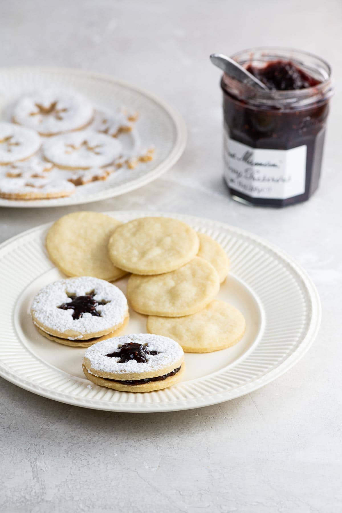 shortbread linzer cookies on plates with a jar of jam