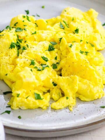 scrambled eggs with parsley and a fork on a grey plate on a light background