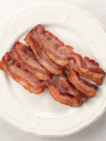 four slices of perfectly crisp thick cut bacon cooked in the oven on a plate