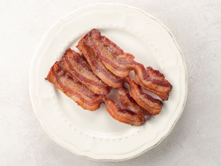 four slices of perfectly crisp thick cut bacon cooked in the oven on a plate