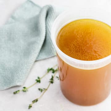 instant pot chicken stock in a quart container with thyme and a dishtowel