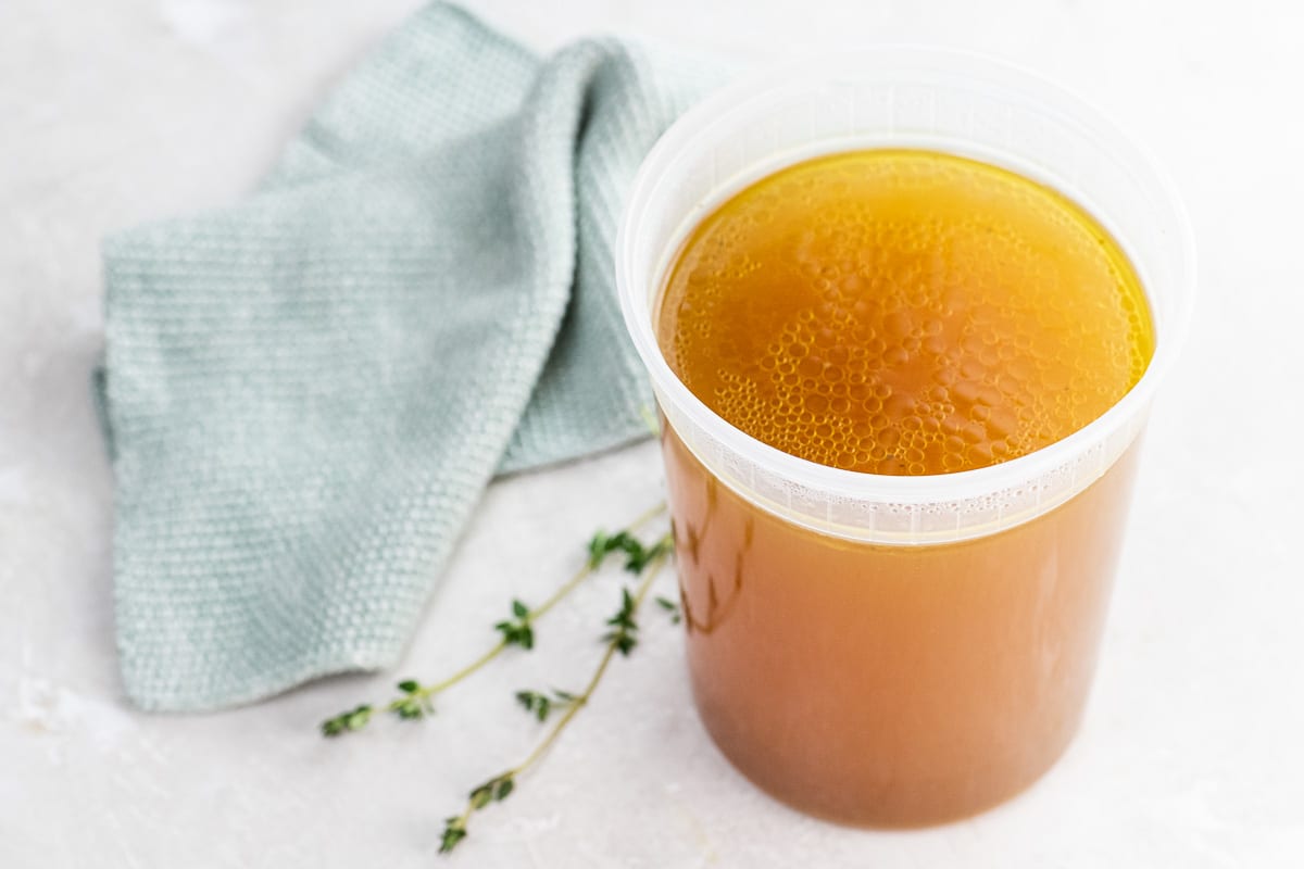 instant pot chicken stock in a quart container with thyme and a dishtowel