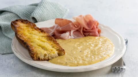 soft and custardy french scrambled eggs, prosciutto slices, and a toasted, buttered baguette piece on a plate