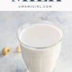 homemade cashew milk in a glass with raw cashews on a surface