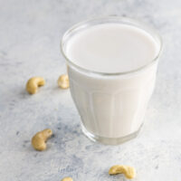 homemade cashew milk in a glass with raw cashews on a surface